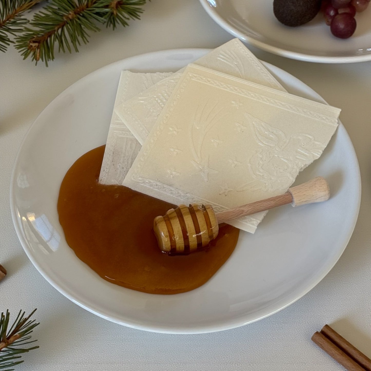 Opłatek wigilijny z miodem na talerzu drewniana pałeczka do miodu tradycja Bożego Narodzenia