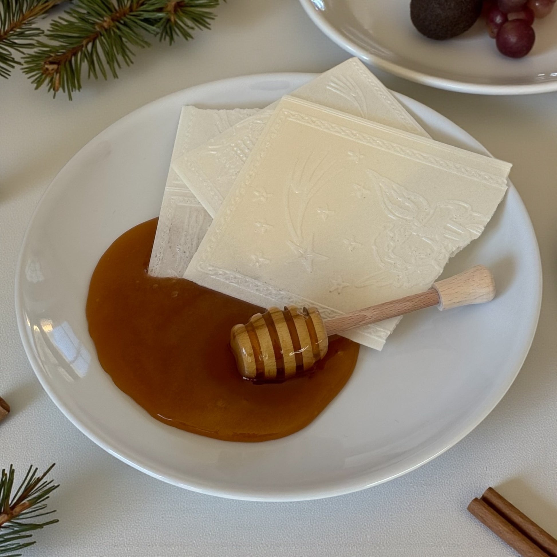 Opłatek wigilijny z miodem na talerzu drewniana pałeczka do miodu tradycja Bożego Narodzenia
