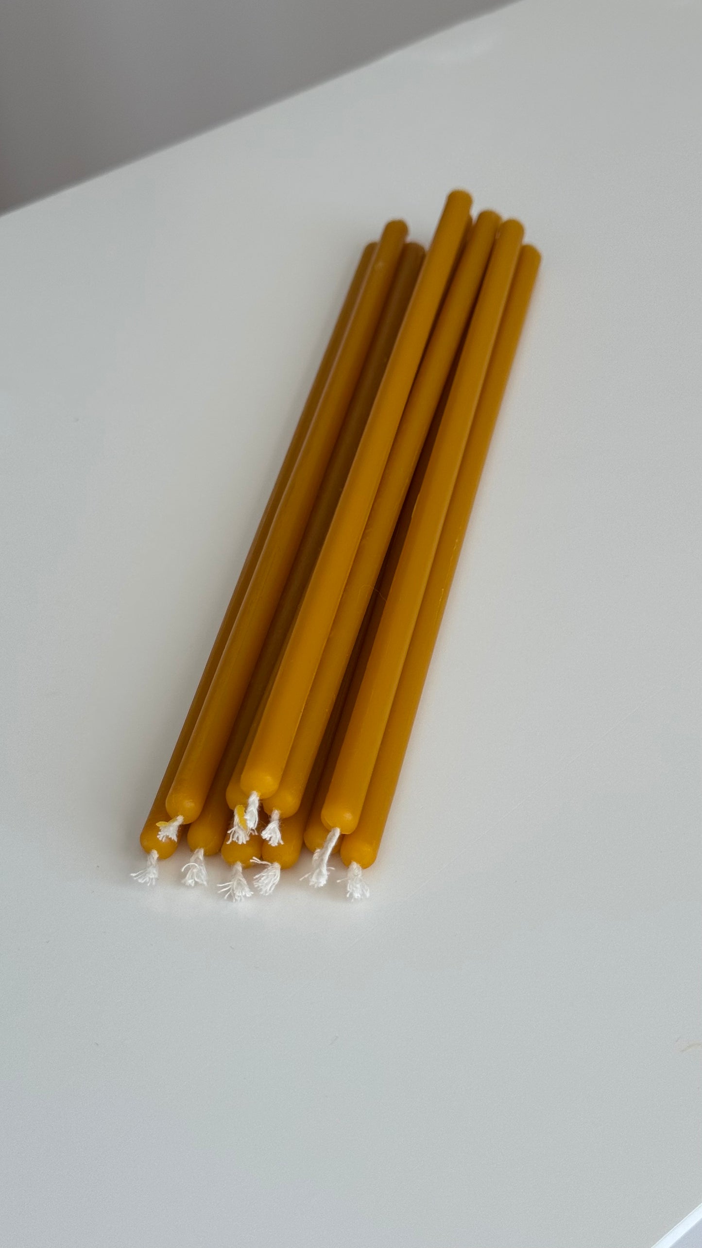 Świece cerkiewne z wosku pszczelego 100% APIMEL – cienkie, żółte świece ułożone na białym tle.